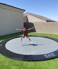 child jumping on a black round inground trampoline
