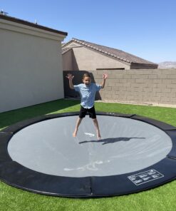 child jumping on a black round inground trampoline