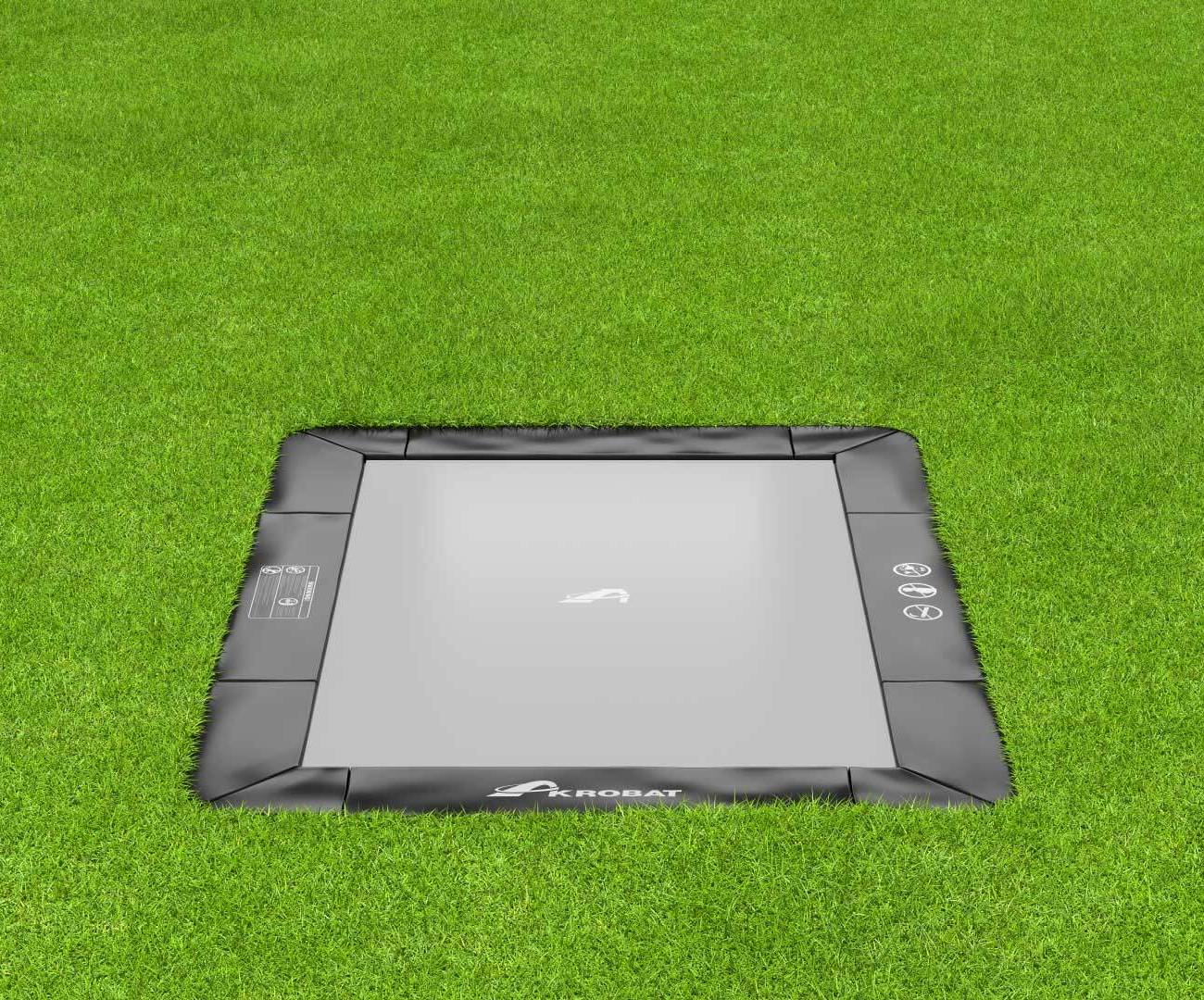 10ft x 6ft Akrobat Primus Flat In-Ground Trampoline - Black Pad with Gray Jump Mat 1 A square trampoline set on vibrant grass, perfect for jumping and enjoying outdoor activities.