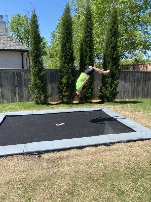 14ft x 10ft Akrobat Primus Flat In-Ground Trampoline - Anthracite Grey (Grey Pad and Black Jump Mat) 2 child doing a trick on a gray rectangular inground trampoline