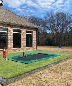 A young child happily jumping on a trampoline in a sunny backyard filled with green grass.