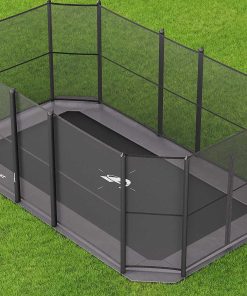 A black trampoline sits on green grass, surrounded by a vibrant green fence.