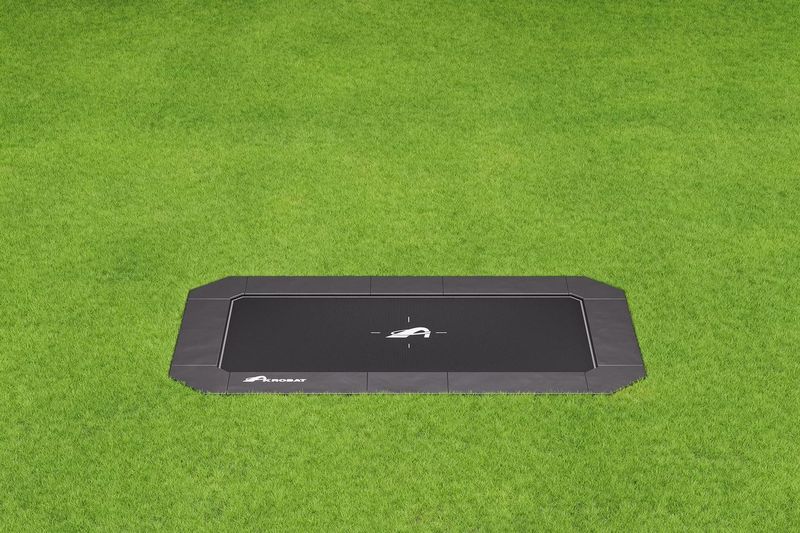 17ft x 10ft Akrobat Primus Flat PLUS In-Ground Trampoline - Special Edition (Black Pad with Black Mat) 1 A black trampoline located on a lush green field, ideal for outdoor fun and exercise.