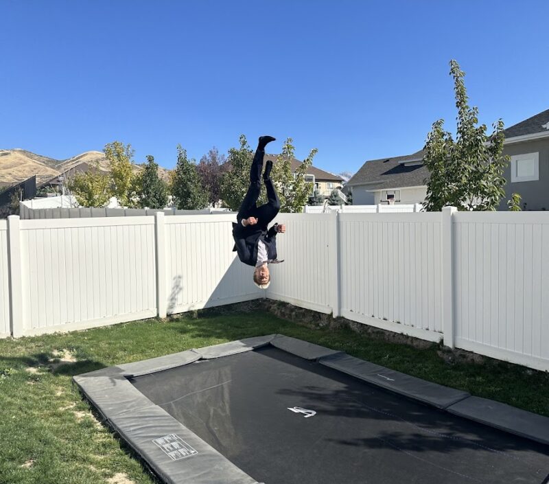 A man executing a flip on a trampoline in a backyard, capturing a moment of excitement and physical skill in nature.