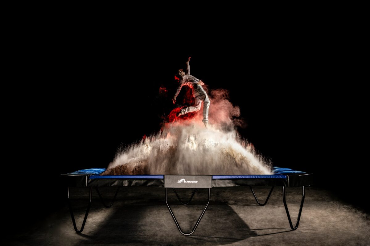 Akrobat 17ft x 12ft XcityX Trampoline Changes the Rules! 1 A man in mid-air on a trampoline, with smoke emanating from it, illustrating a lively and playful atmosphere.