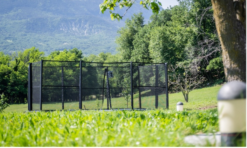 Essential Safety Certificates Your Trampoline Should Have 8 A black metal cage with a central fence stands isolated in a vast green field under a clear blue sky.