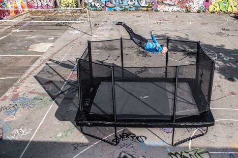 Akrobat’s Trampoline Frame Has a Lifetime Warranty 1 A man leaps into the air on a trampoline in a lively park setting, enjoying a moment of fun and exercise.